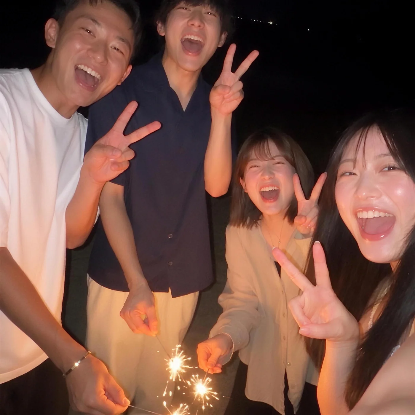 夜の砂浜で線香花火をする男女4人
